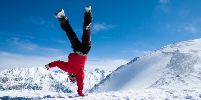 Someone doing a one-handed handstand high in the snowy mountains